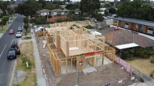 Aerial view of a residential house under construction with wooden framing and scaffolding in a suburban neighborhood.